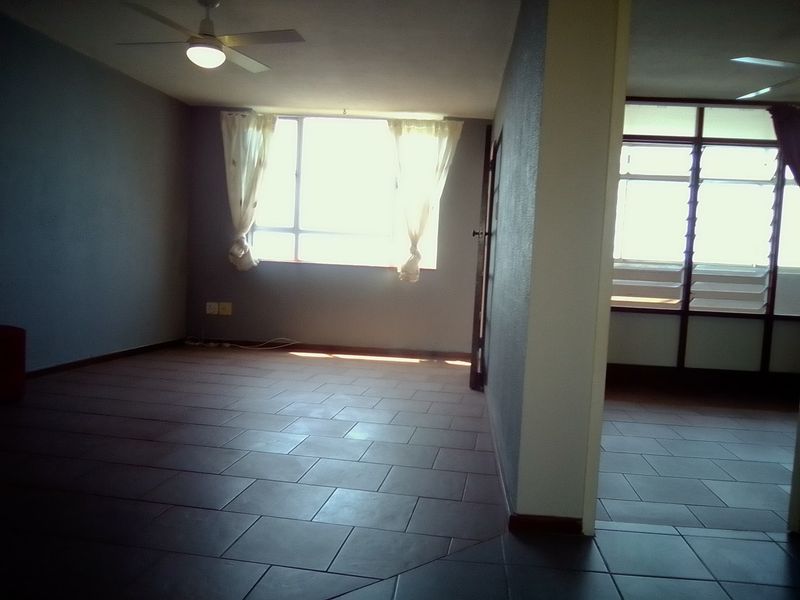 An empty living area featuring tiled flooring, a ceiling fan, and natural light from large windows.