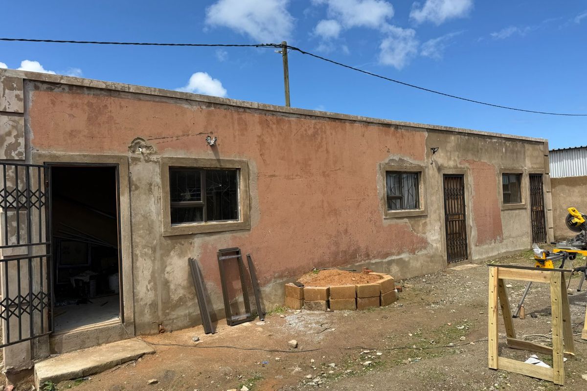 Rear exterior view of the property showing weathered plaster walls, security gates, and aluminium window frames in need of maintenance and finishing.