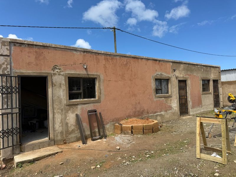 Rear exterior view of the property showing weathered plaster walls, security gates, and aluminium window frames in need of maintenance and finishing.