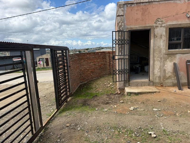 Exterior view of a property featuring a metal security gate, brick boundary wall, and a building with weathered exterior finishes and security door access.