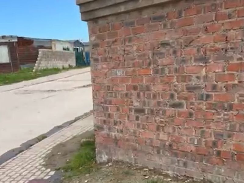 A street-level view showing a weathered brick boundary wall adjacent to a concrete road and paved verge.