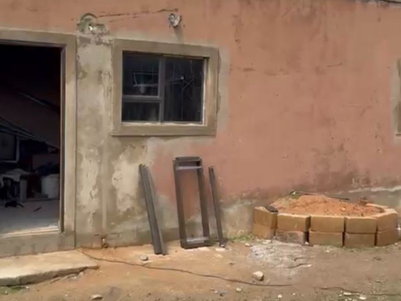 Exterior view of a residential building showing weathered plastered walls, a window frame, and an unfinished entrance area.