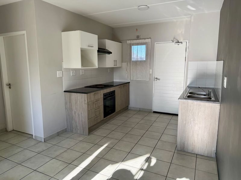 A clean, functional kitchen featuring light wood-look cabinetry, dark countertops, built-in oven and hob, and neutral tiled flooring.