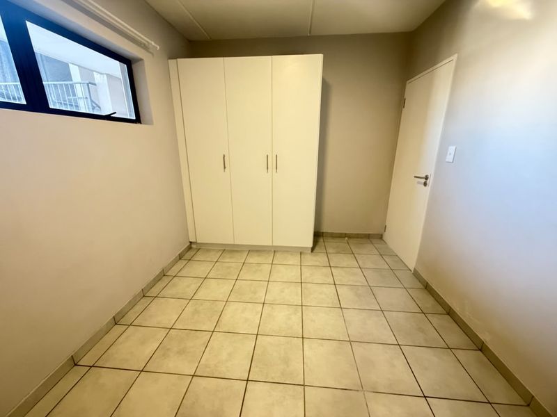 A clean, empty bedroom featuring neutral tiled flooring, a built-in white wardrobe, and a window providing natural light.