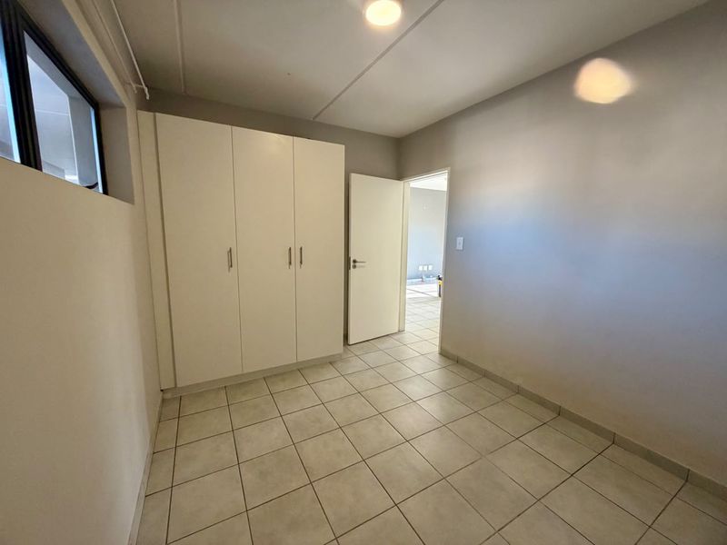A clean, empty bedroom featuring neutral tiled flooring and built-in cupboards, offering a versatile space ready for personalization.