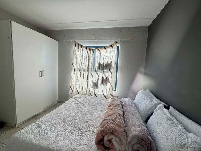 A bedroom featuring a built-in wardrobe and tiled flooring, showing signs of wear on the wall surfaces requiring maintenance.