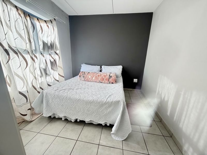 A bedroom featuring tiled flooring and a dark grey accent wall, providing a neutral base for personalization.