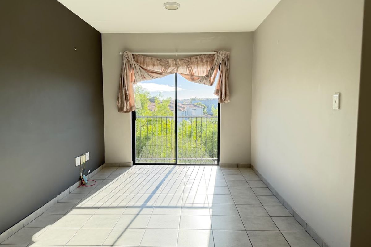 An empty living room featuring tiled flooring and a sliding glass door that opens to a balcony with neighborhood views.