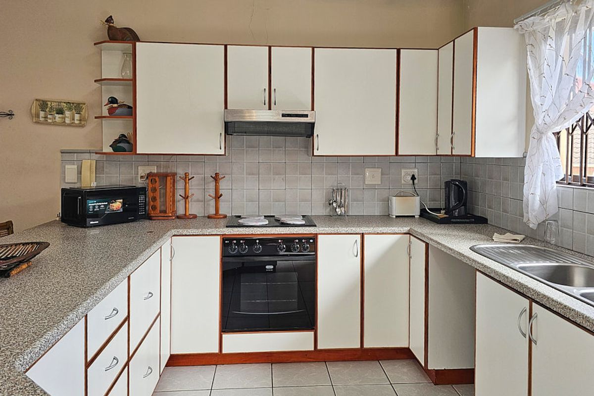 Functional kitchen featuring white cabinetry, laminate countertops, tiled backsplash, built-in oven, hob, extractor fan, and a double bowl stainless steel sink.