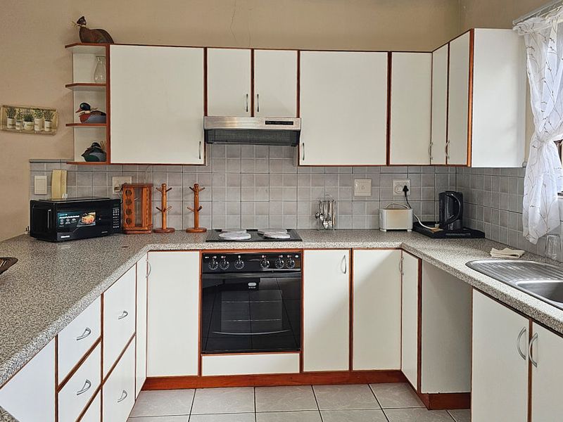 Functional kitchen featuring white cabinetry, laminate countertops, tiled backsplash, built-in oven, hob, extractor fan, and a double bowl stainless steel sink.