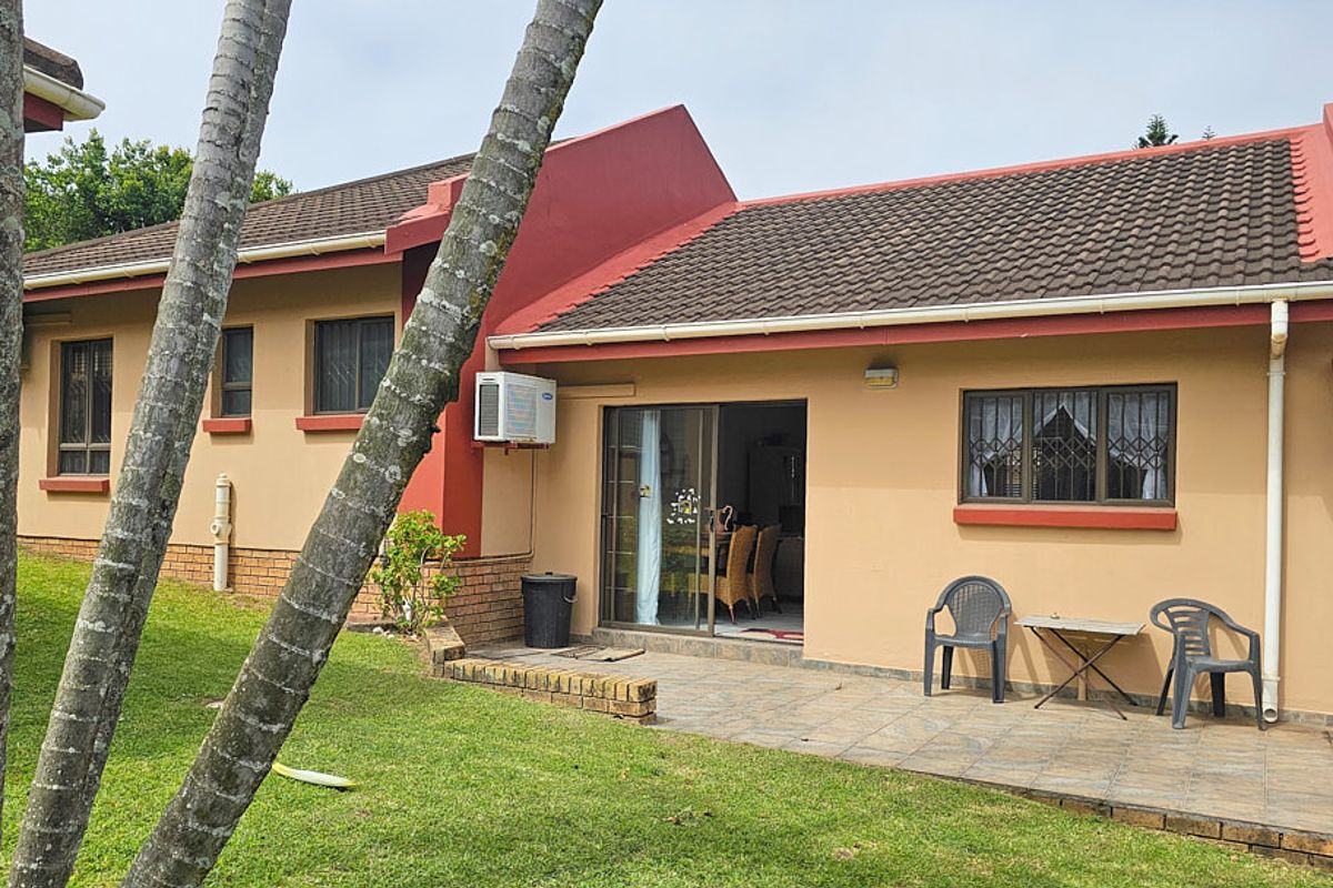 Rear view of the townhouse featuring a tiled patio area, sliding glass door access, and an external air conditioning unit set against a lawn.