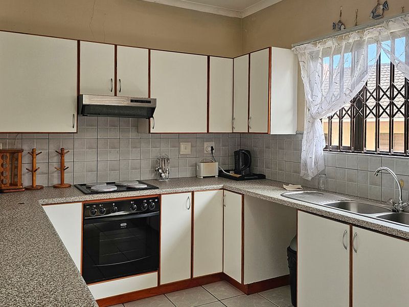 Functional kitchen featuring white cabinetry, laminate countertops, tiled backsplash, and integrated appliances, including an electric hob, oven, and extractor fan.