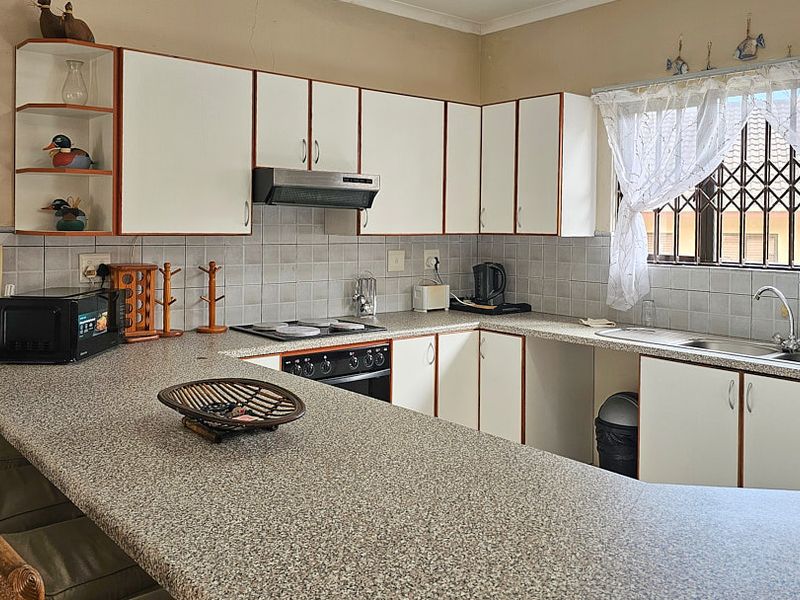 Functional kitchen featuring laminate countertops, built-in cabinetry, electric hob, oven, extractor fan, and a stainless steel sink with a tiled backsplash.