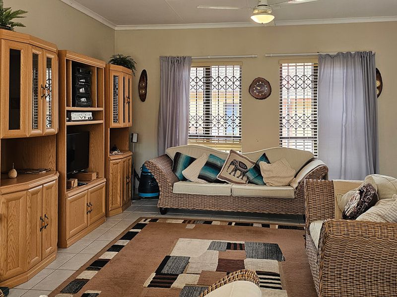 A comfortable living room featuring tiled flooring, a ceiling fan, and large windows fitted with security gates and blinds.