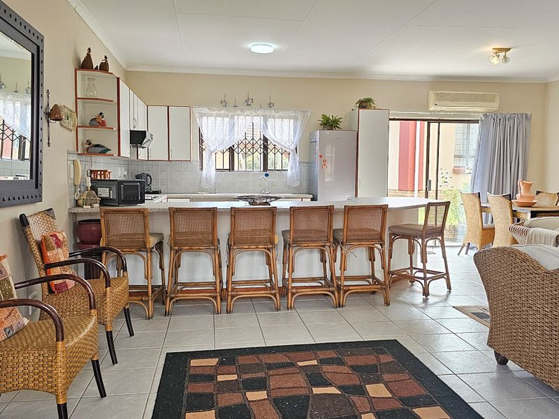 Open plan living and kitchen area featuring tiled flooring, a breakfast bar, and direct access to the outdoor space via sliding glass doors.
