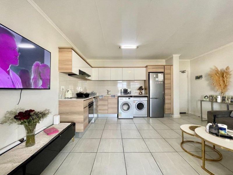 Open-plan living area featuring a modern kitchen with built-in cabinetry, integrated laundry appliances, and tiled flooring throughout.