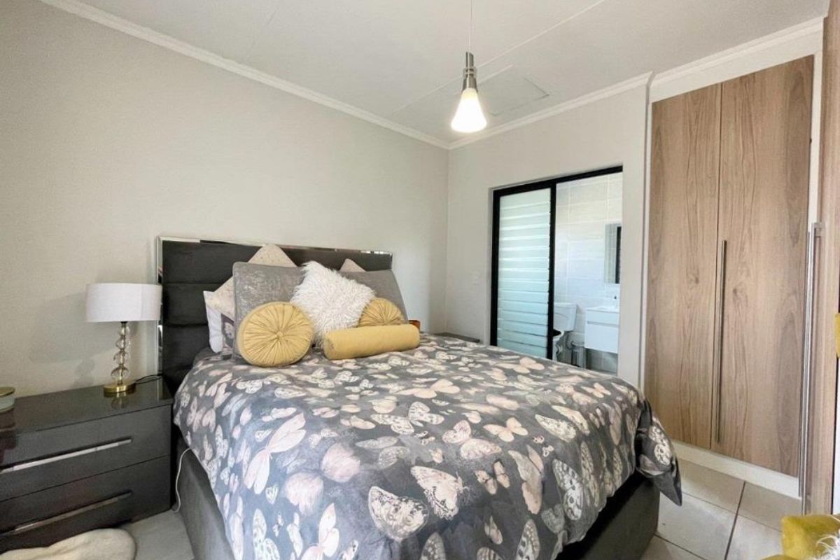 A well-maintained bedroom featuring built-in wooden cupboards, tiled flooring, and direct access to an en-suite bathroom through a sliding door.