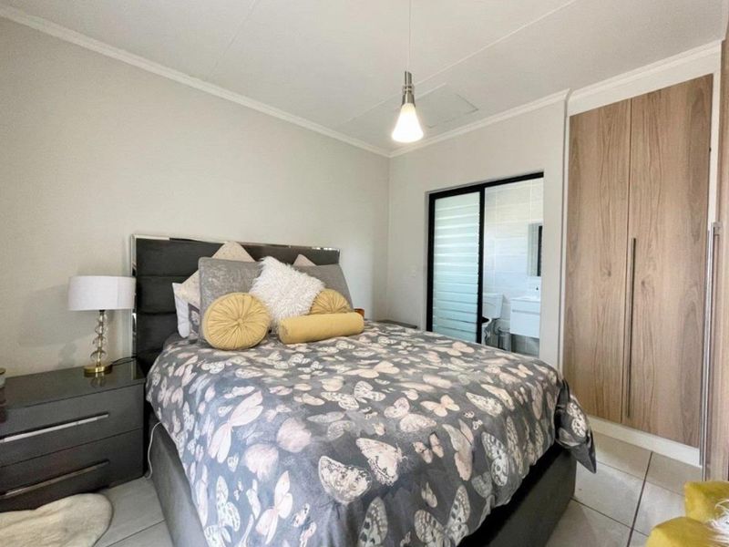 A well-maintained bedroom featuring built-in wooden cupboards, tiled flooring, and direct access to an en-suite bathroom through a sliding door.