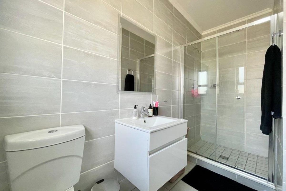 Modern bathroom featuring a wall-mounted vanity, glass shower enclosure, and neutral ceramic tiling throughout.