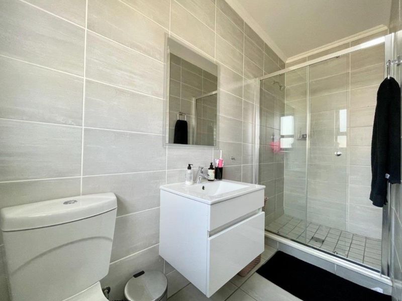 Modern bathroom featuring a wall-mounted vanity, glass shower enclosure, and neutral ceramic tiling throughout.