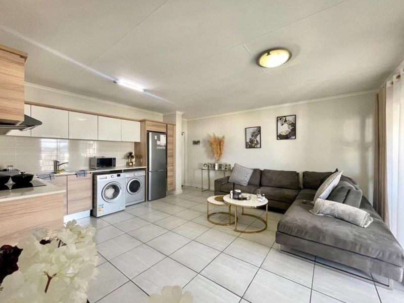 Modern open-plan living area featuring a well-appointed kitchen with built-in cabinetry, tiled flooring, and integrated appliances, seamlessly flowing into the comfortable lounge space.