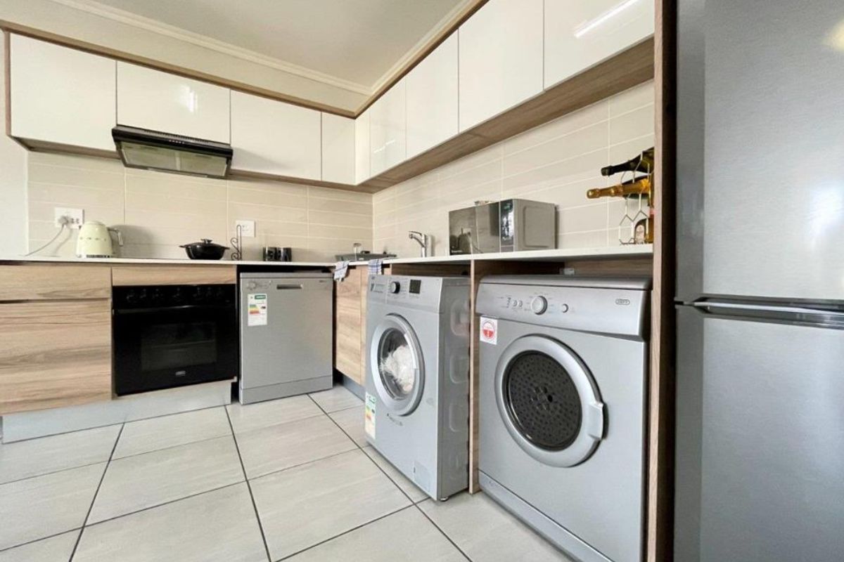 Modern kitchen featuring sleek white and wood-tone cabinetry, tiled backsplash, integrated oven, extractor fan, and dedicated spaces for laundry appliances.