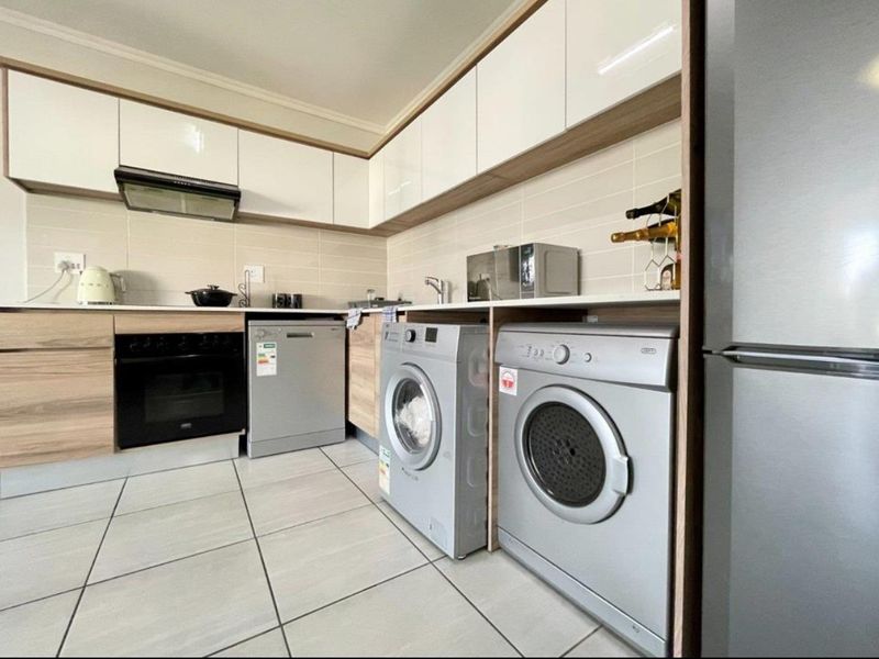 Modern kitchen featuring sleek white and wood-tone cabinetry, tiled backsplash, integrated oven, extractor fan, and dedicated spaces for laundry appliances.