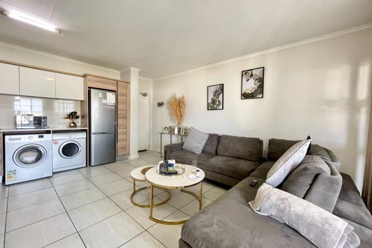 Open-plan living area featuring tiled flooring and a compact kitchen with built-in cabinetry and integrated laundry facilities.