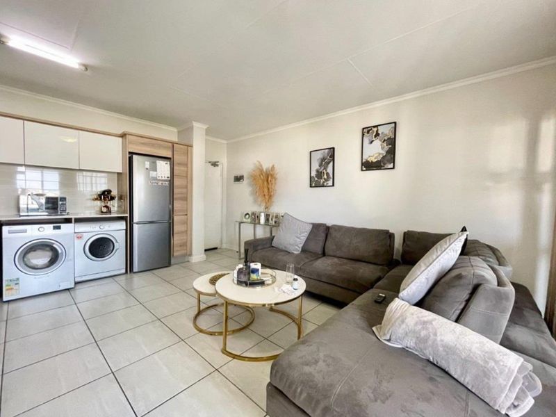 Open-plan living area featuring tiled flooring and a compact kitchen with built-in cabinetry and integrated laundry facilities.