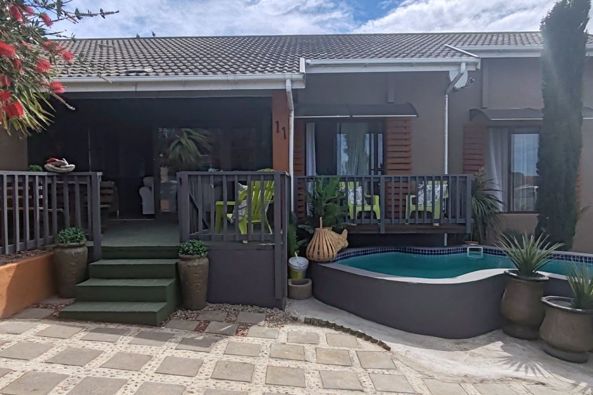Rear exterior view featuring a raised timber deck, paved patio area, and a built-in swimming pool with tiled finish.