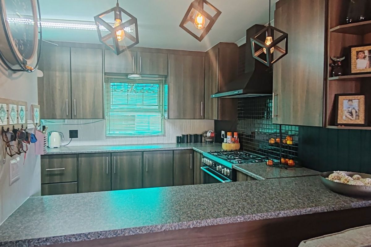 Modern kitchen featuring dark wood cabinetry, granite countertops, a gas hob with extractor fan, and stylish pendant lighting.