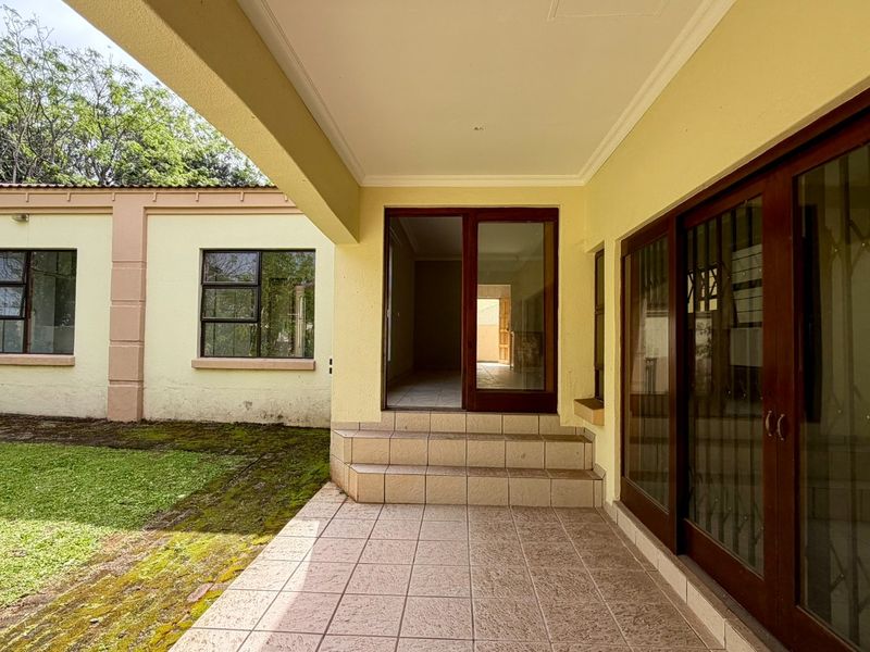 A covered patio area featuring tiled flooring and sliding glass doors, providing direct access to the garden and interior living spaces.