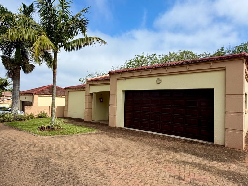 Front exterior view of a townhouse featuring a paved driveway, double garage, and well-maintained stucco facade under a tiled roof.