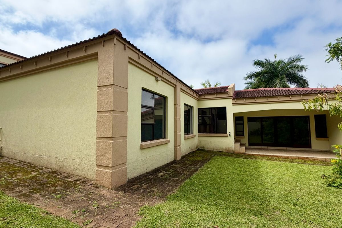 Rear view of the townhouse featuring a covered patio, paved walkway, and established garden area with tiled roof architecture.