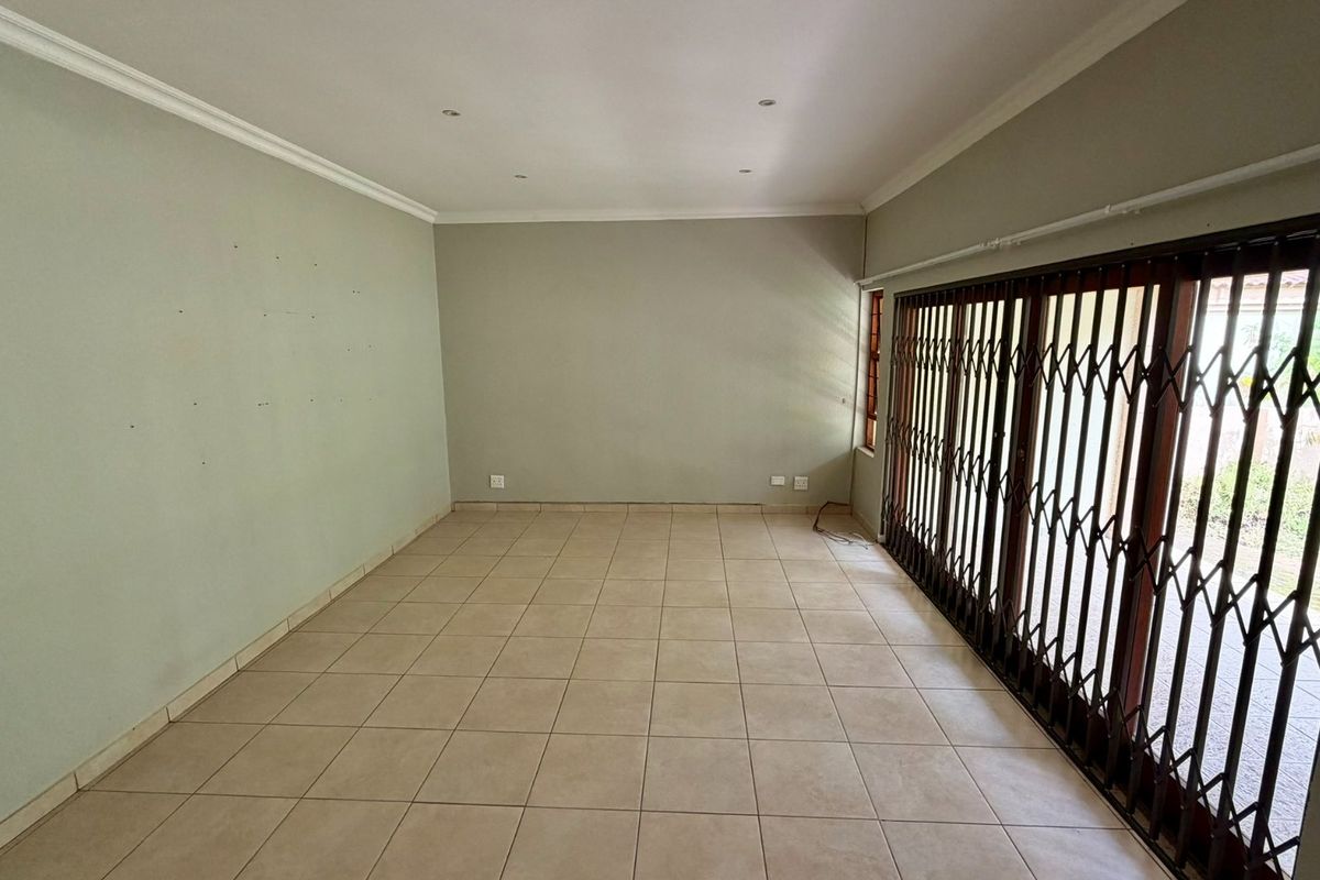 An empty, neutrally painted living room featuring tiled flooring, recessed lighting, and large sliding glass doors with a security gate leading to the exterior.