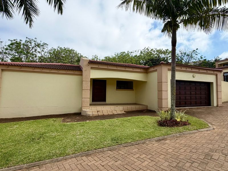 Front elevation of a townhouse featuring a paved driveway, double garage, and a landscaped front lawn with a covered entrance.