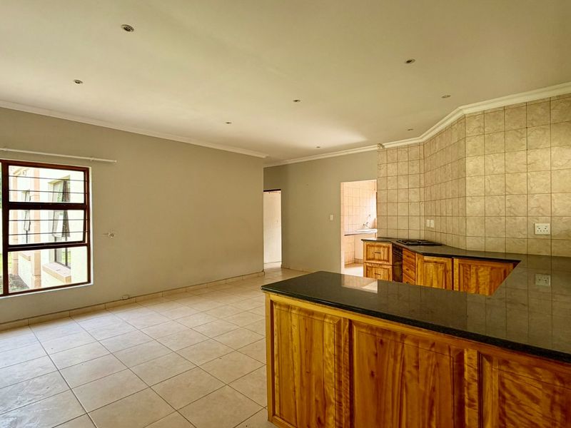 Spacious open-plan living and kitchen area featuring wooden cabinetry, granite countertops, tiled flooring, and recessed lighting, offering a functional and versatile layout.
