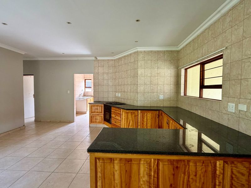 Spacious open-plan kitchen featuring wooden cabinetry, granite countertops, and built-in appliances, seamlessly flowing into the living area with neutral tiled flooring.