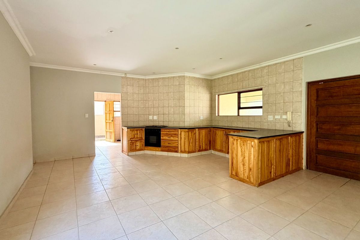 Spacious kitchen featuring wooden cabinetry, built-in oven, tiled splashbacks, and stone countertops, offering a functional layout in an open-plan setting.