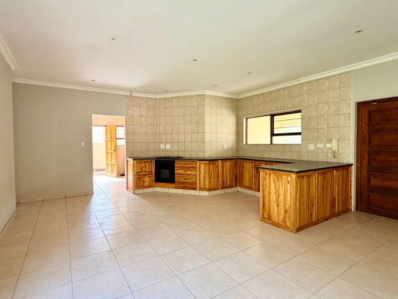 Spacious kitchen featuring wooden cabinetry, built-in oven, tiled splashbacks, and stone countertops, offering a functional layout in an open-plan setting.