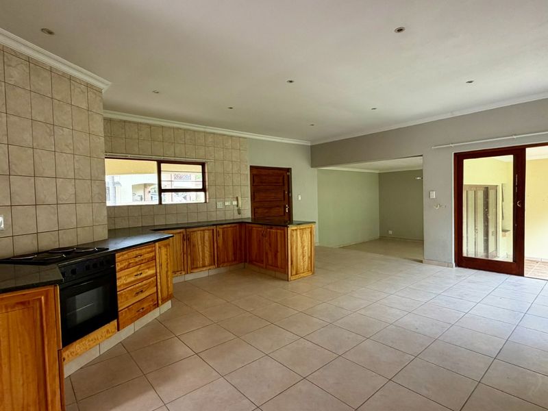 Spacious open-plan kitchen and living area featuring wooden cabinetry, granite countertops, built-in oven, tiled flooring, and direct access to an outdoor patio.