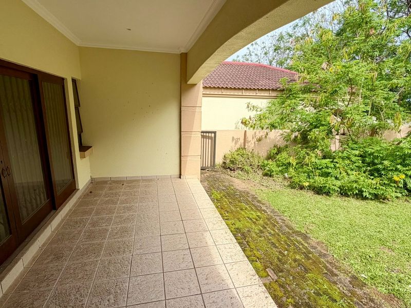 A covered patio area featuring tiled flooring and sliding glass doors, overlooking a private garden with a boundary wall.