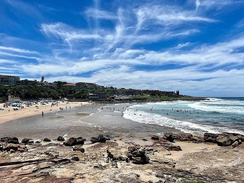 A scenic coastal view overlooking a sandy beach, rocky shoreline, and the ocean with residential properties visible along the coastline.