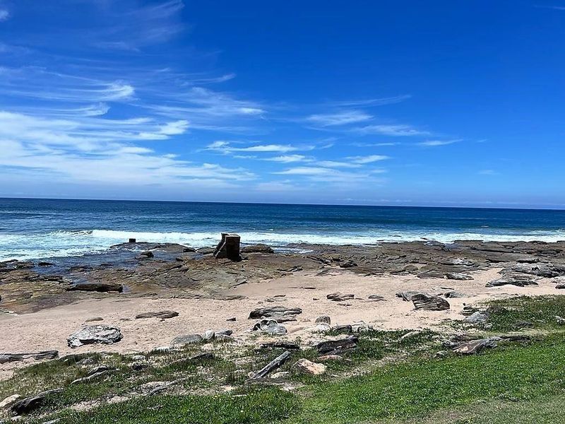 A scenic coastal view featuring a rocky shoreline, sandy beach, and the ocean under a clear blue sky.