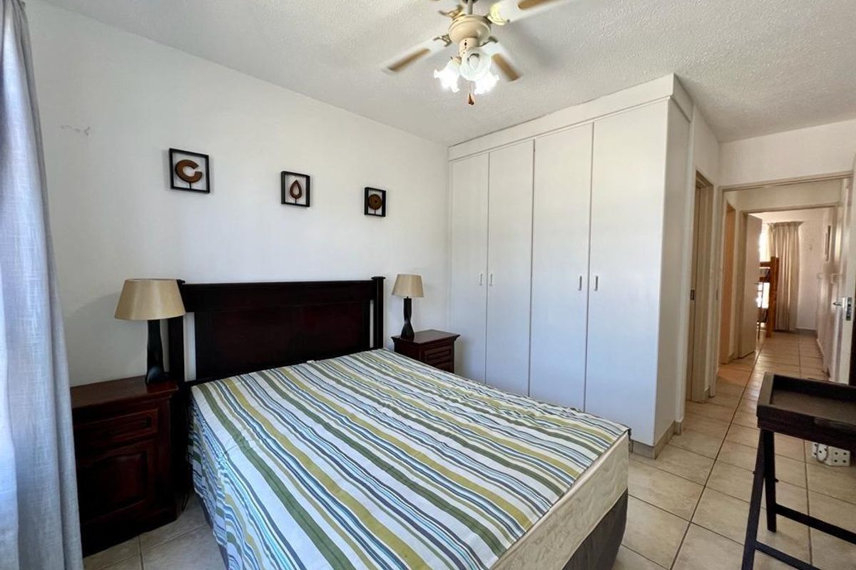 A functional bedroom featuring built-in cupboards, a ceiling fan, and tiled flooring, offering a clean and practical living space.