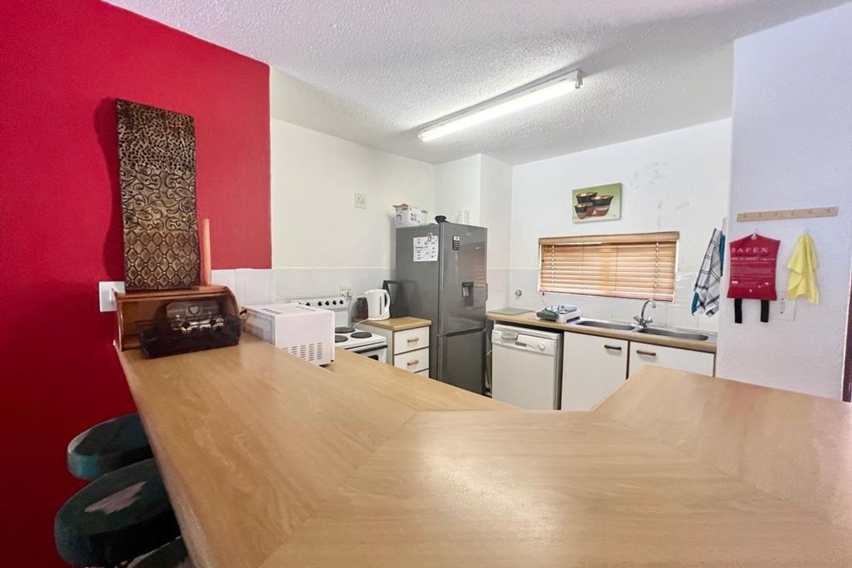 A functional kitchen featuring a built-in breakfast bar, double basin sink, and tiled splashback, offering a practical layout for daily meal preparation.