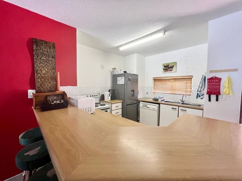 A functional kitchen featuring a built-in breakfast bar, double basin sink, and tiled splashback, offering a practical layout for daily meal preparation.