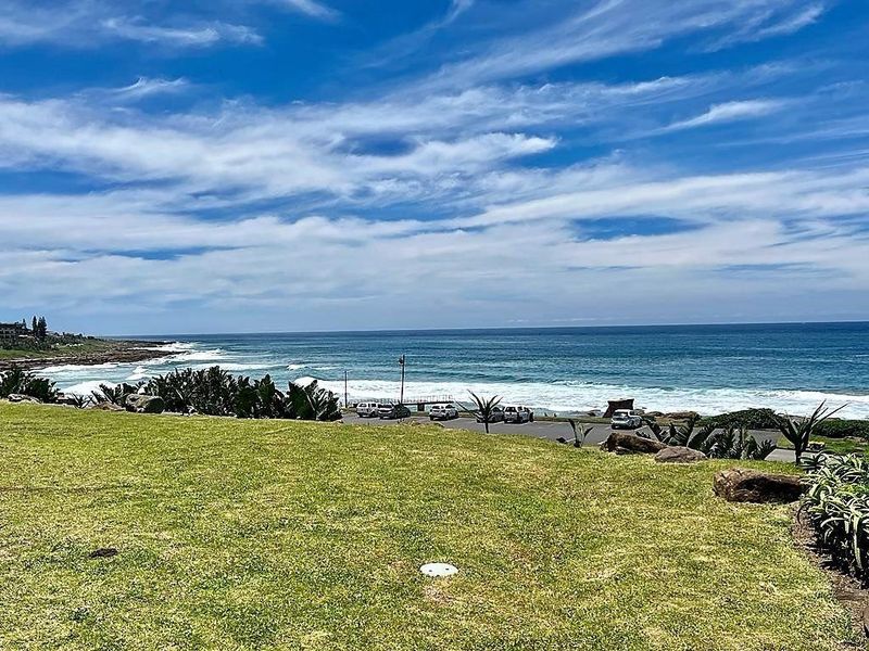 A scenic coastal view overlooking the ocean, featuring a well-maintained grassy lawn in the foreground.