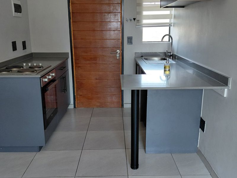 A compact, modern kitchen featuring grey cabinetry, stone countertops, a built-in oven, electric hob, and tiled flooring.