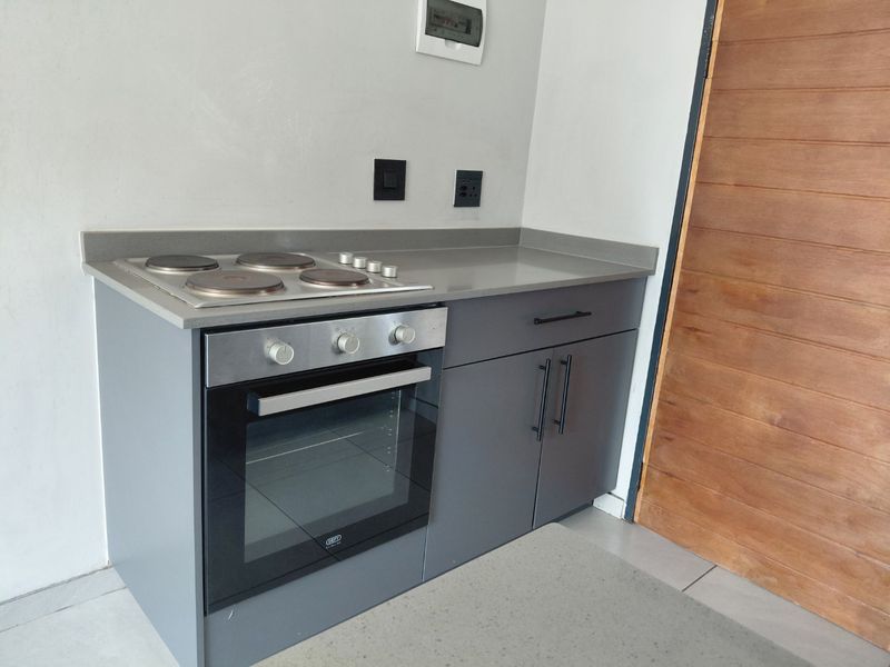 A modern, compact kitchen area featuring grey cabinetry, a stone countertop, and a built-in electric oven and hob.